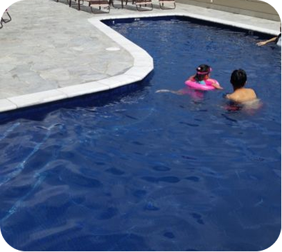 Two people swimming in a blue pool beside a light-colored deck