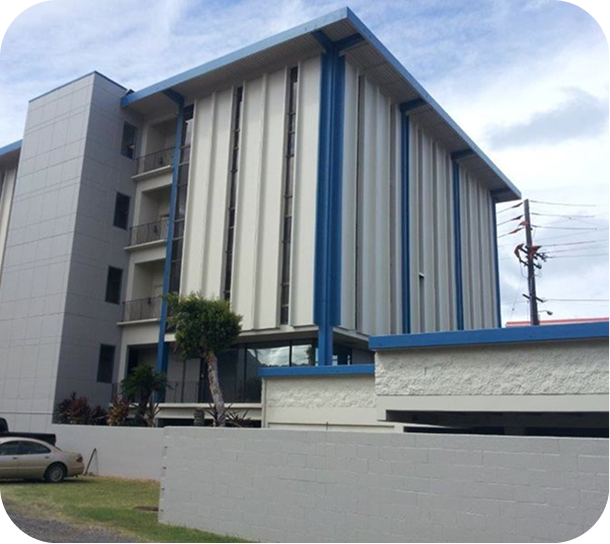Modern multi-story building with blue and beige exterior, seen behind a low white wall.