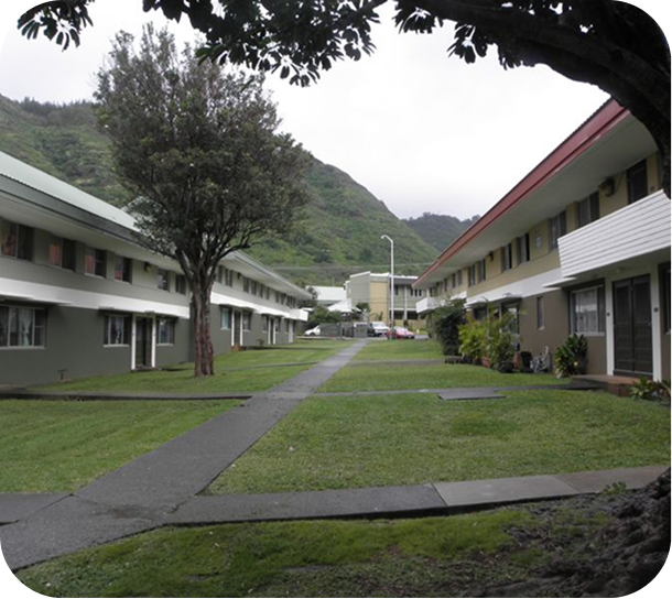 Walkway between two white apartment buildings on a green campus, with mountains in the background.
