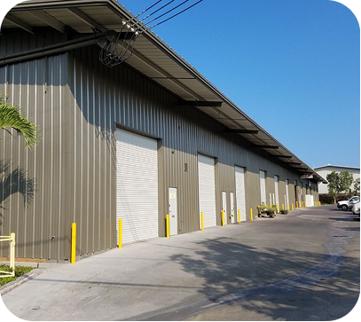 Industrial warehouse building with corrugated metal walls, white roll-up doors, and a paved driveway