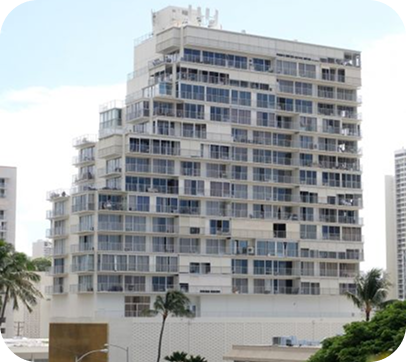Tall white apartment building with many balconies under a cloudy sky, with palm trees in front