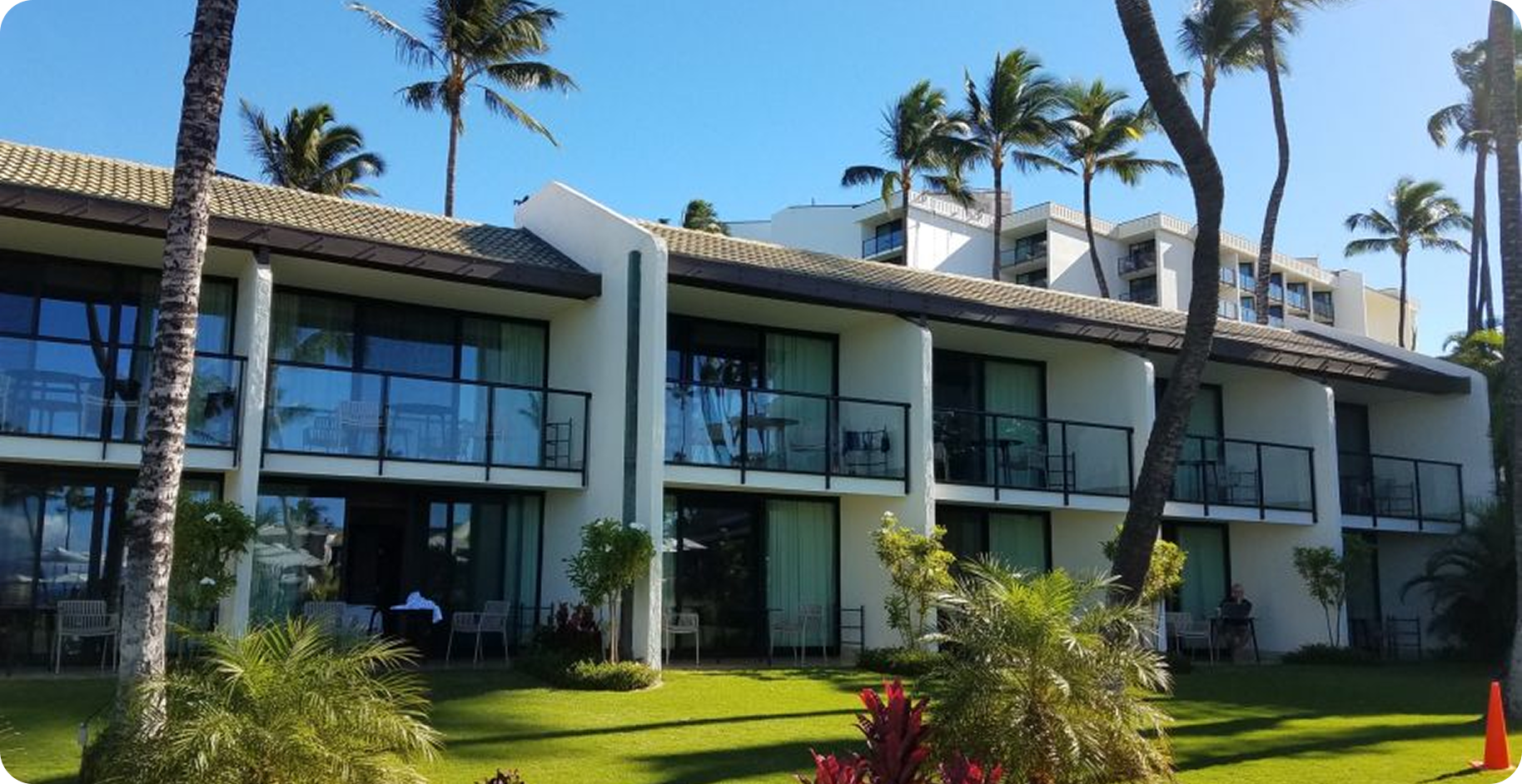 Modern two-story hotel buildings with balconies and palm trees in a sunny tropical resort courtyard