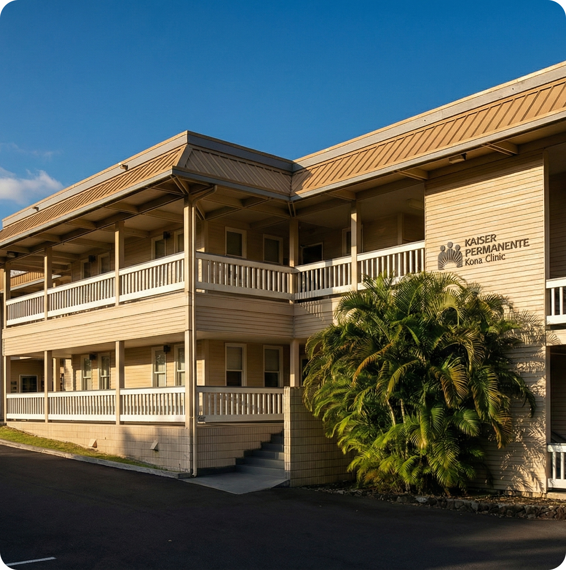 Two-story beige hotel with balconies and palm trees in front, under a clear blue sky