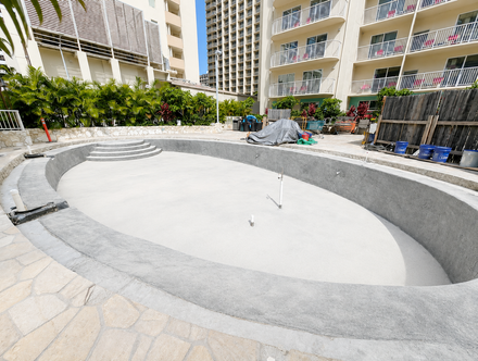 Worker applying white coating to a flat rooftop with a roller, leaving a sharp edge over dark roof membrane.