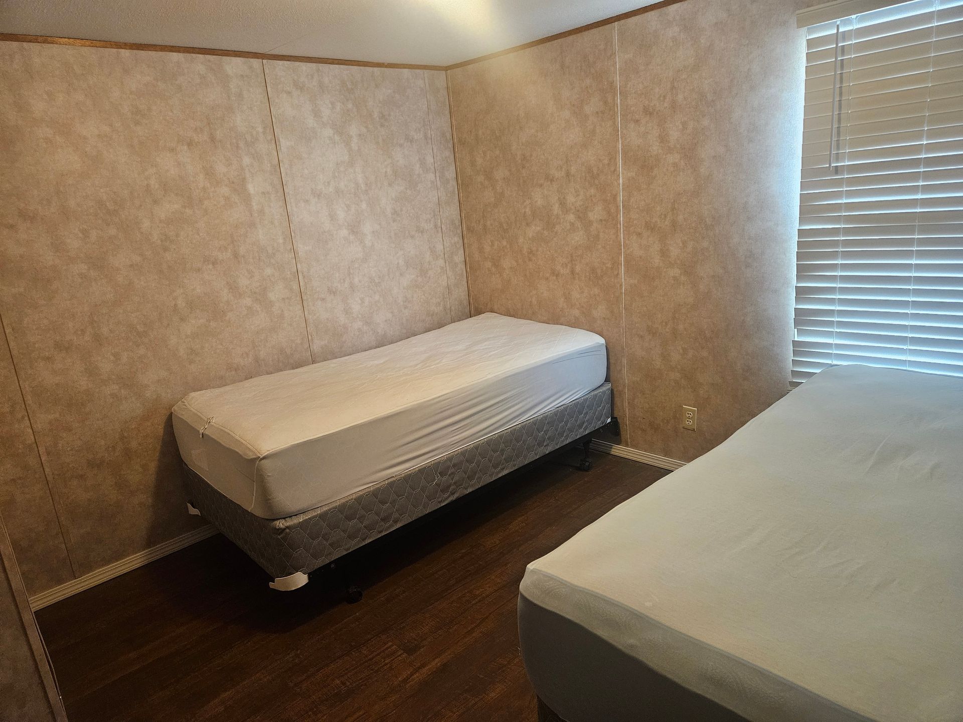 A bedroom with two beds and a window with blinds.