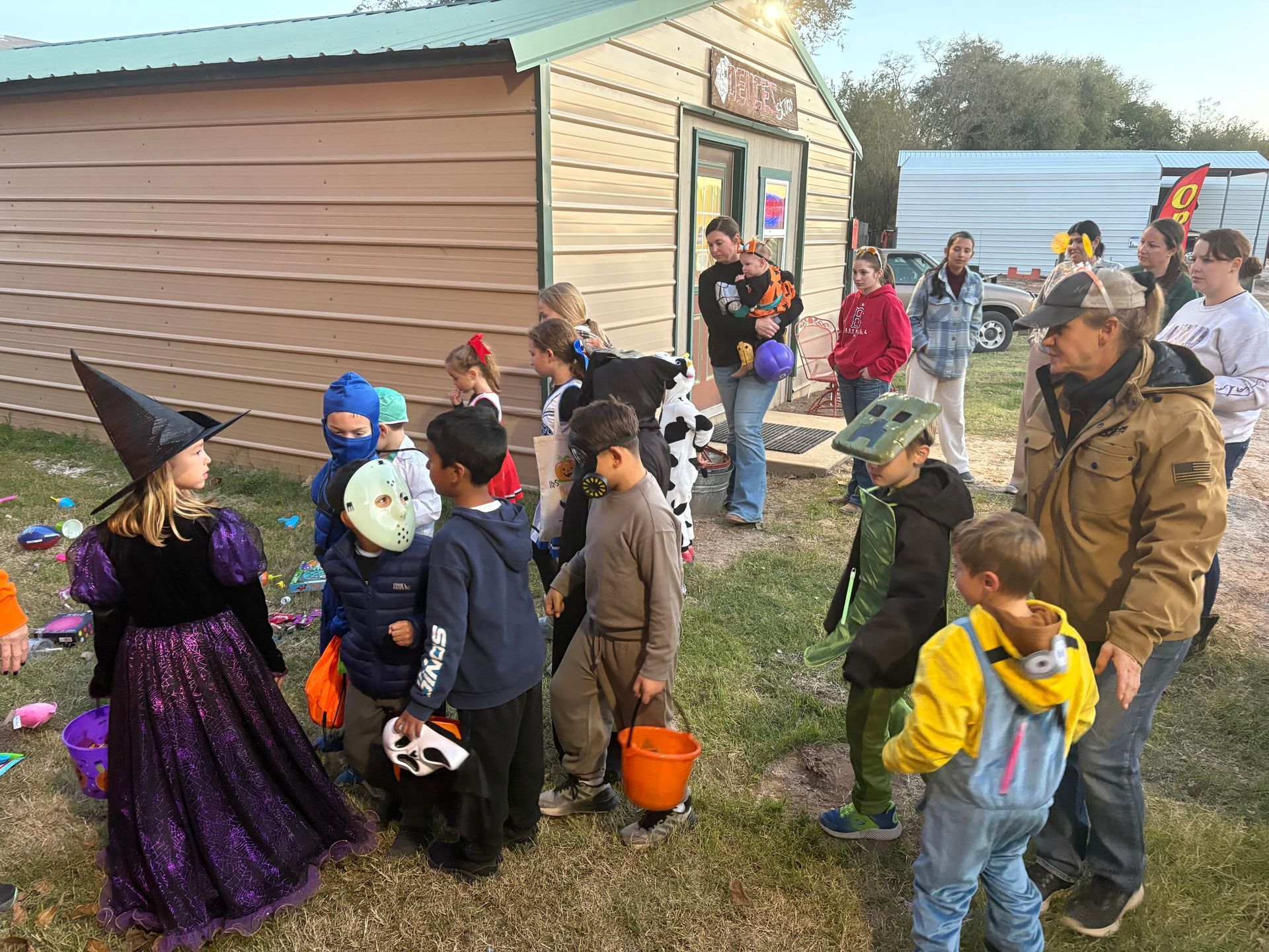 Children in Halloween costumes line up outside a small building, trick-or-treating.
