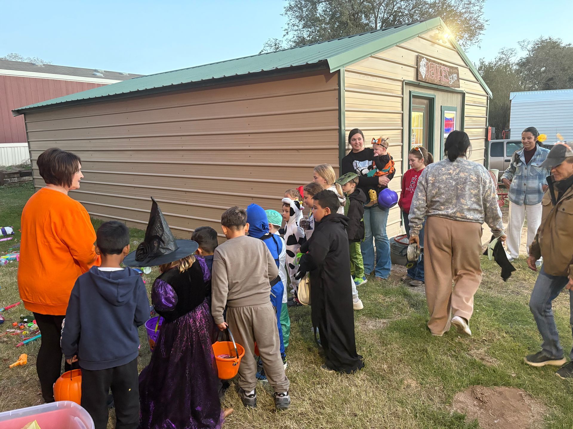 Children in Halloween costumes gather near a building; adults supervise.