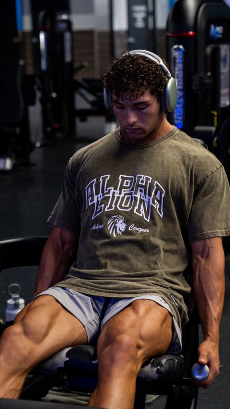 A man wearing headphones is sitting on a bench in a gym.