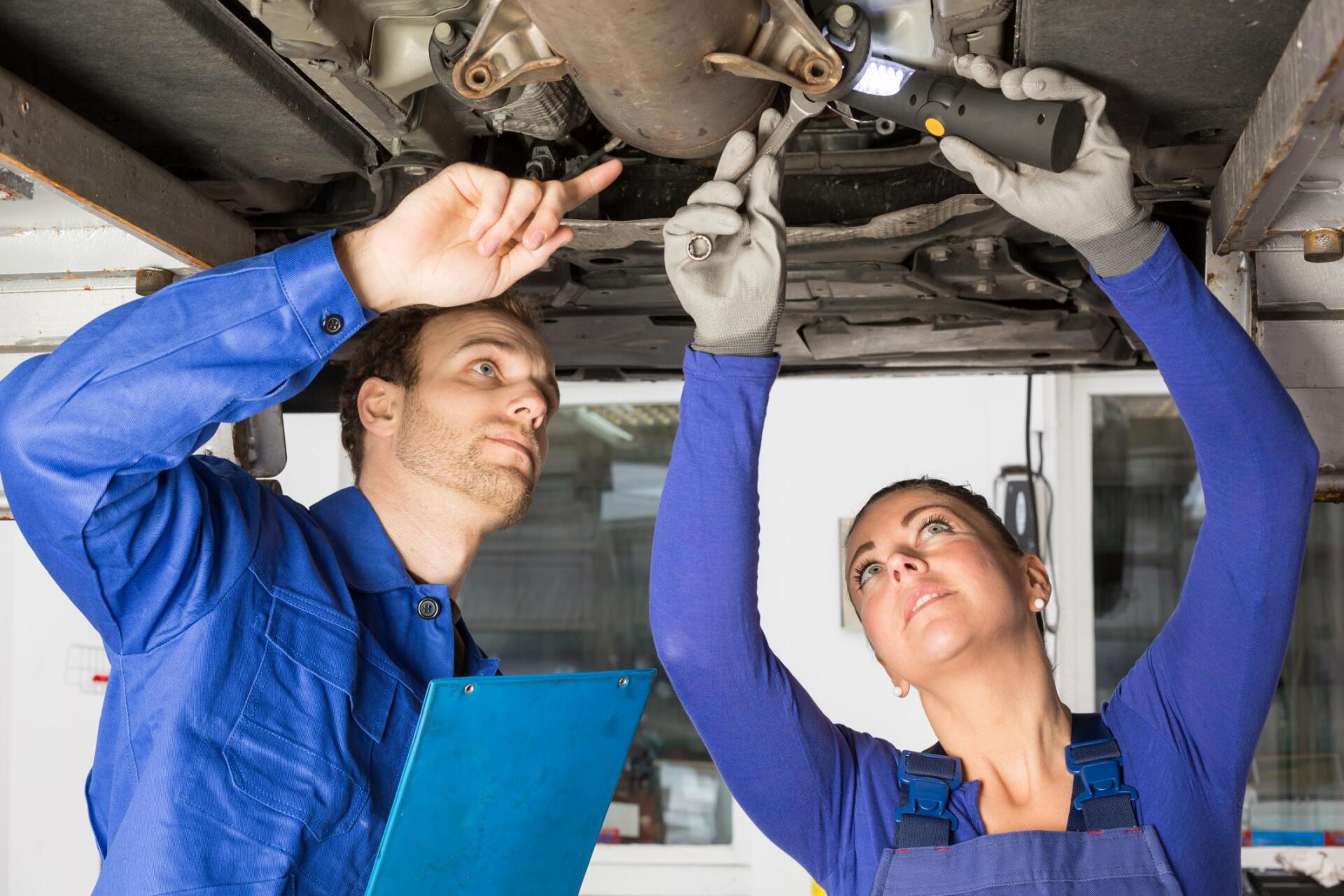 two workers standing below the car