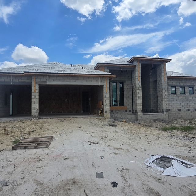 Partially built stone house with garage, unfinished sandy yard, and blue cloudy sky