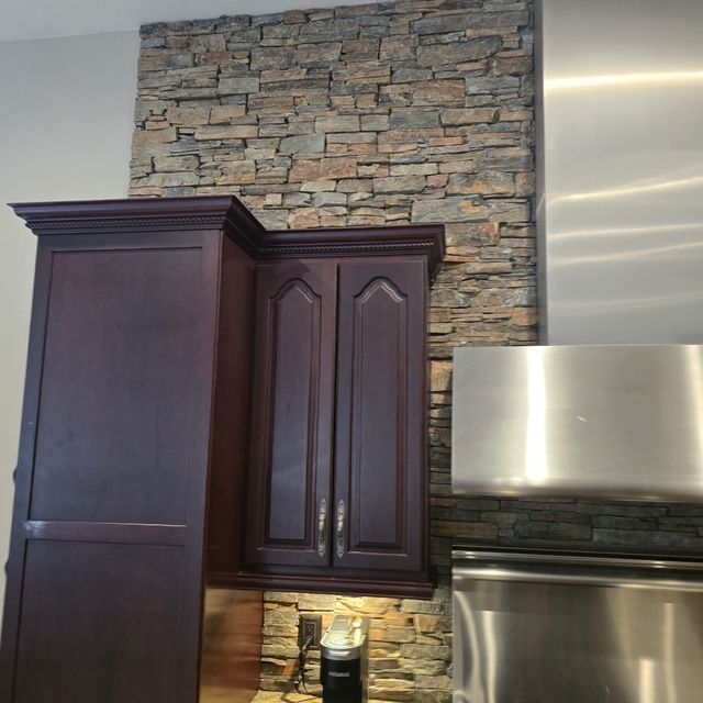 Dark wood kitchen cabinets against a stacked-stone backsplash with stainless steel appliances
