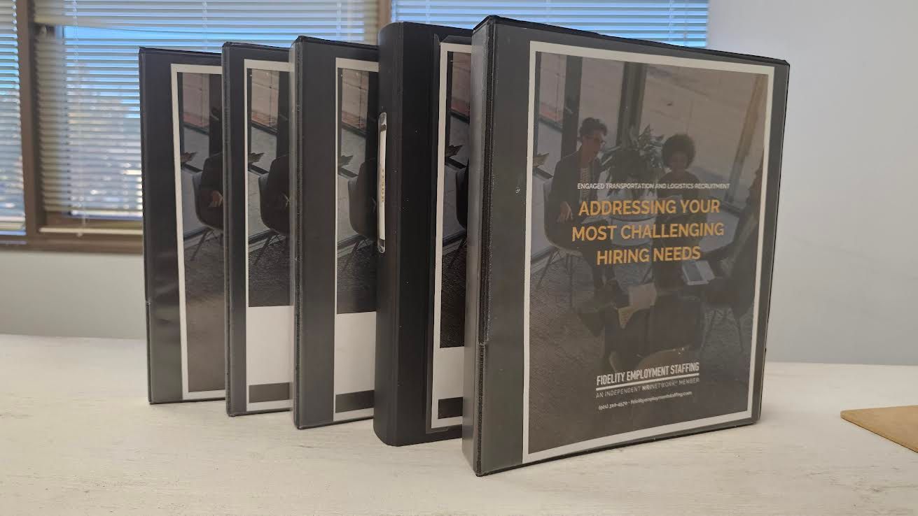 Six black binders on a white table, with a cover that says