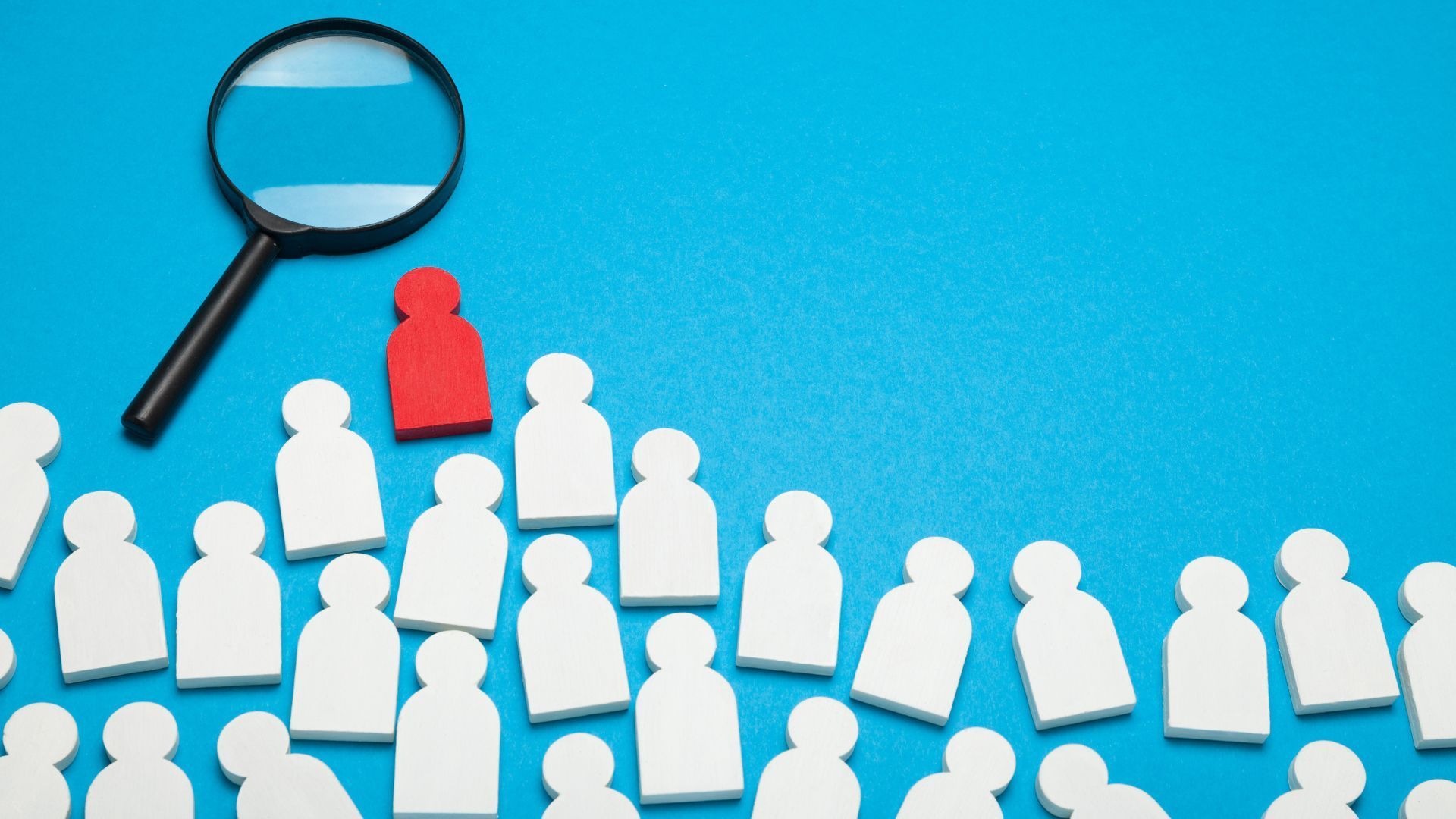 Magnifying glass focused on a red figure among a crowd of white figures on a blue surface.