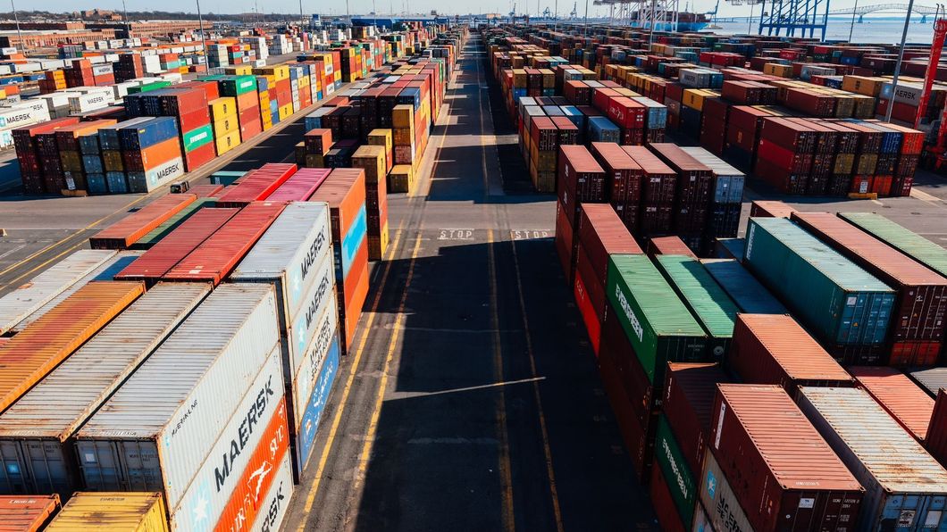 Rows of colorful shipping containers at a port, lined up for transport under a blue sky.