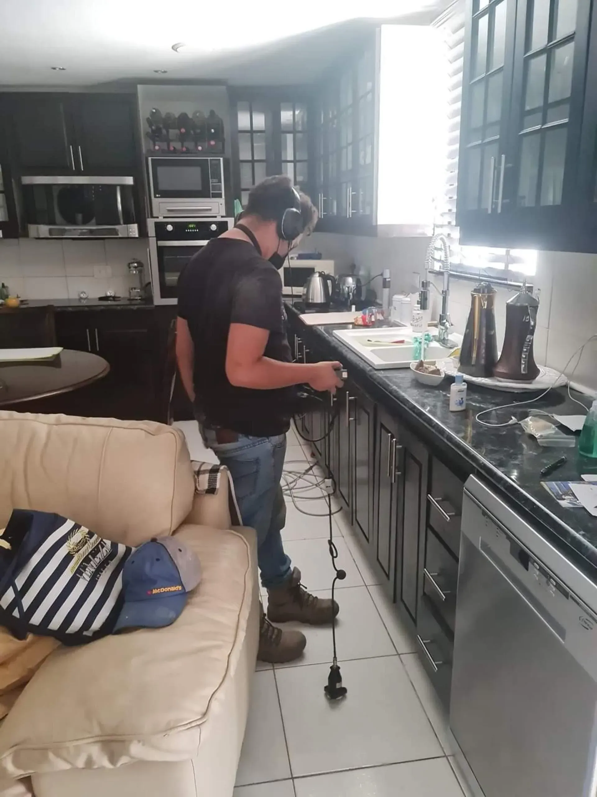 Persona limpiando una encimera de cocina moderna junto a un sofá y electrodomésticos de acero inoxidable.