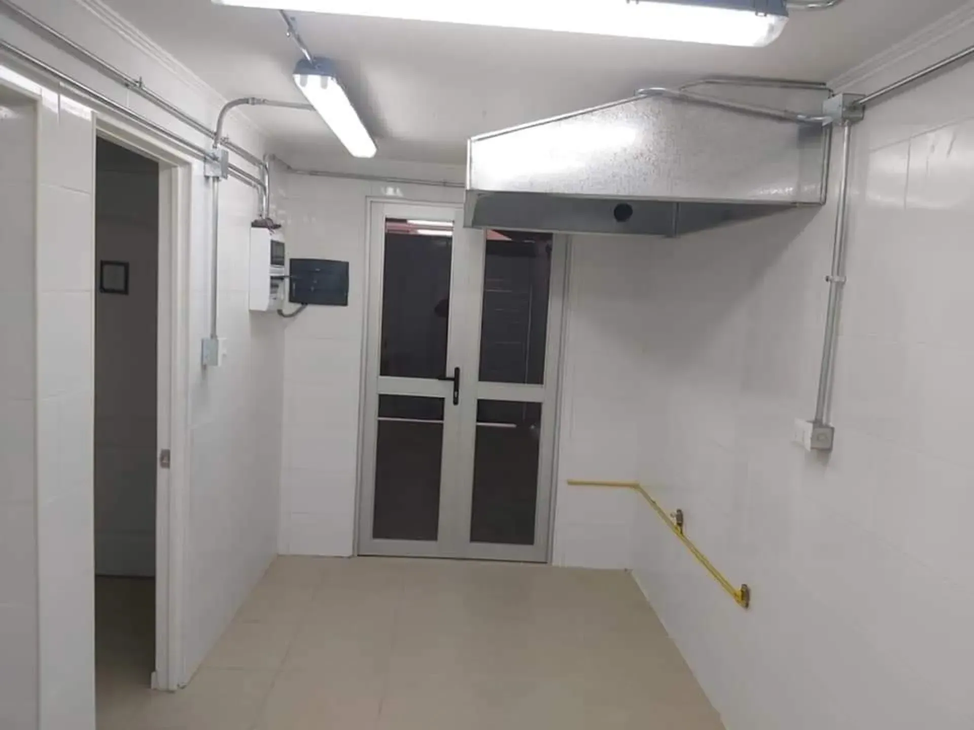 Cuarto de servicio blanco y luminoso con luces fluorescentes, suelo de baldosas y puertas dobles al fondo.