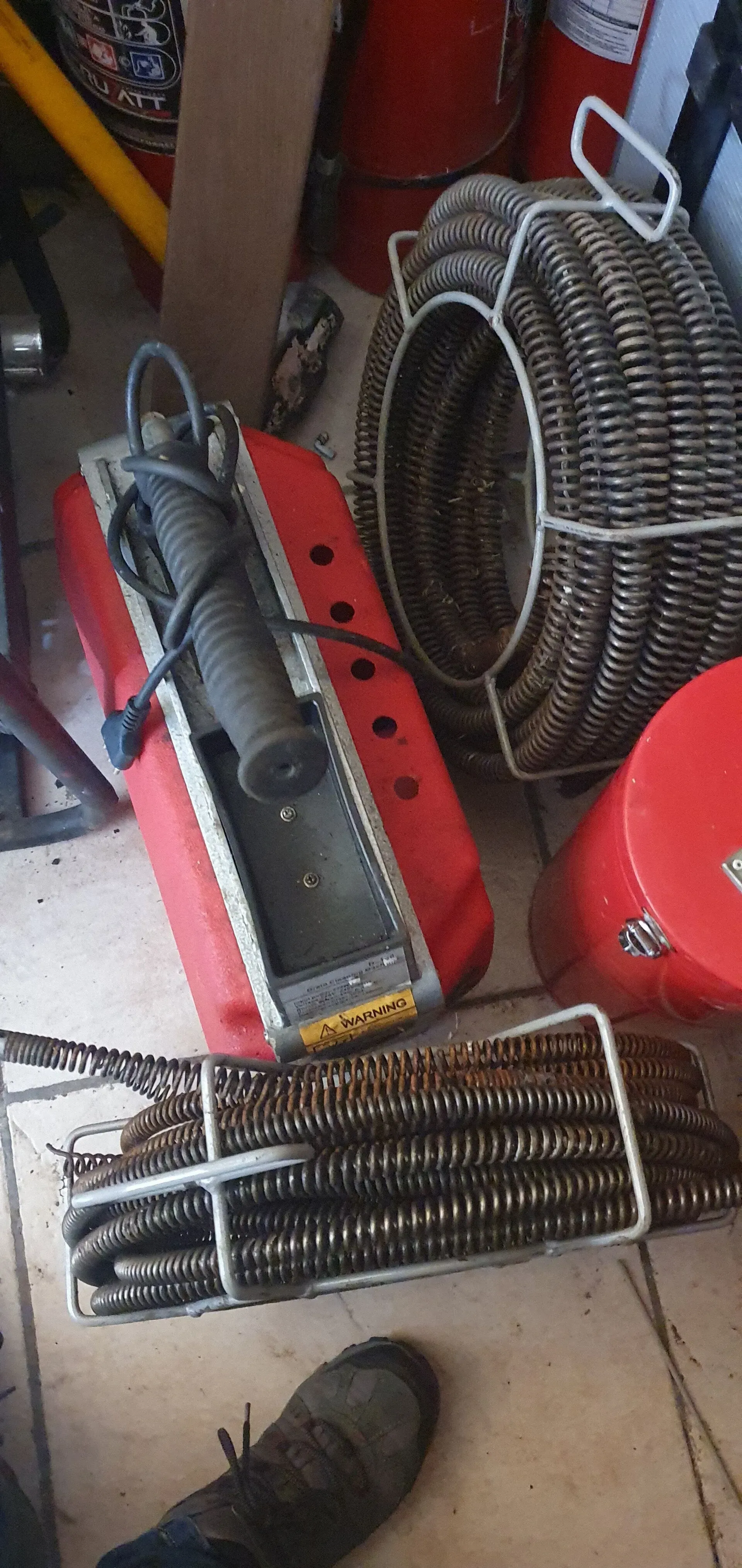 Piezas de un calentador de metal rojo y un ventilador de alambre negro en un suelo desordenado cerca de un ventilador rojo y la pata de una mesa.