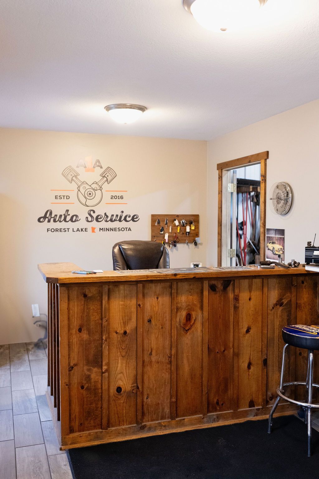 Small reception desk in a beige office with a wood front, stool, wall sign, and mirror.