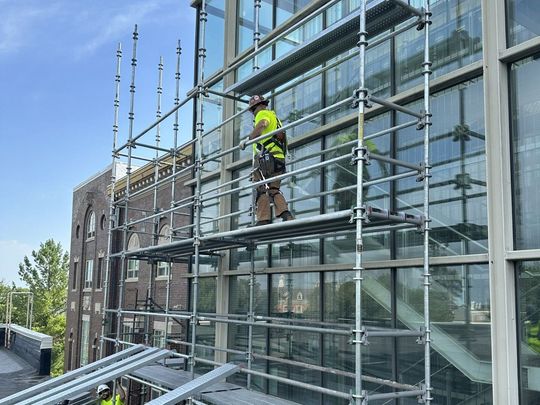 Two construction workers are working on a roof on a scaffolding.