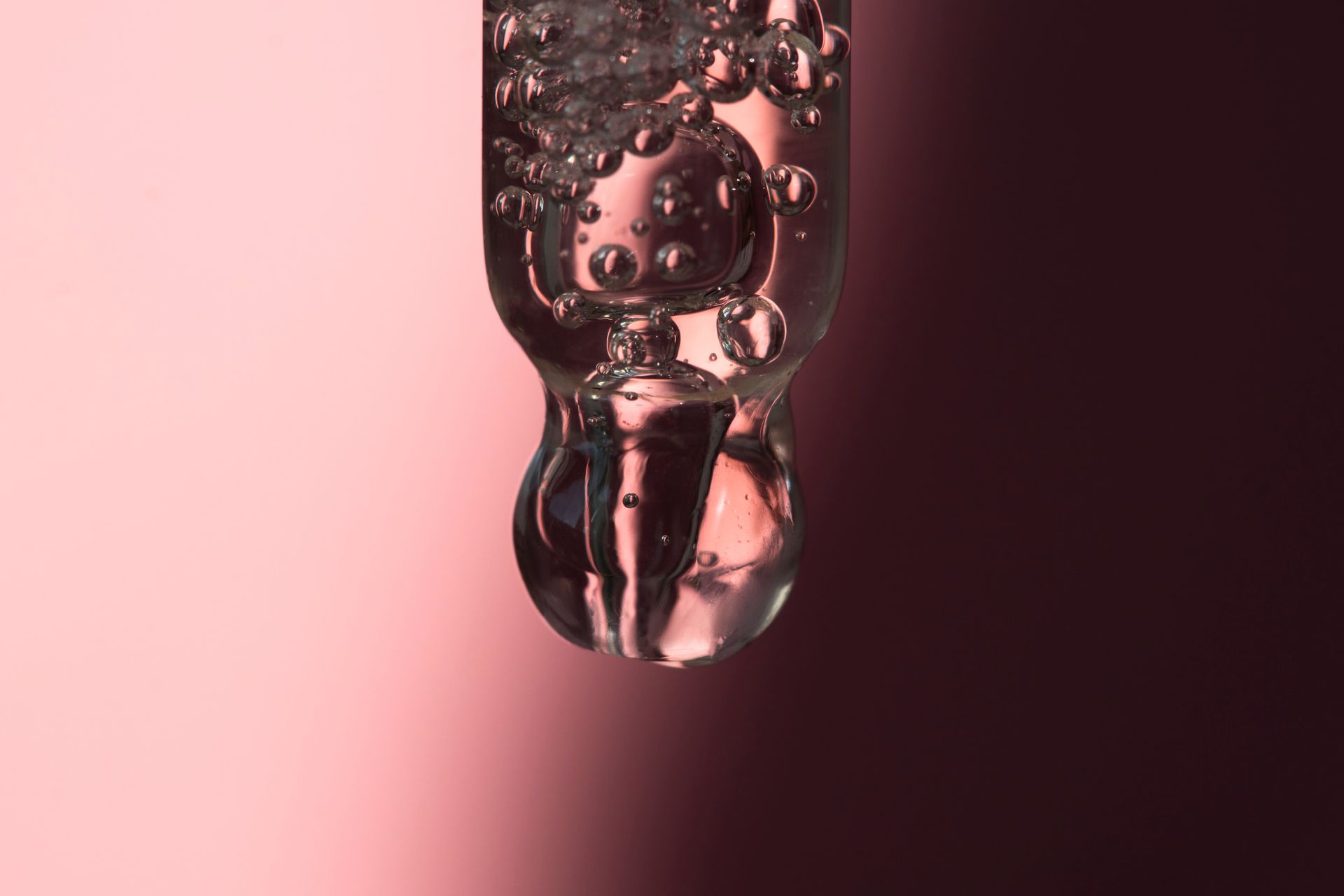 Eine Nahaufnahme eines Flüssigkeitstropfens auf einem rosa Hintergrund.