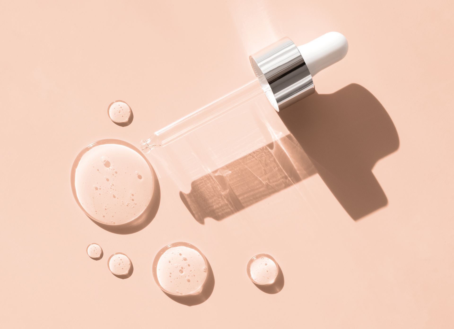 Eine Flasche Serum mit einer Pipette und Serumtropfen auf einem rosa Hintergrund.