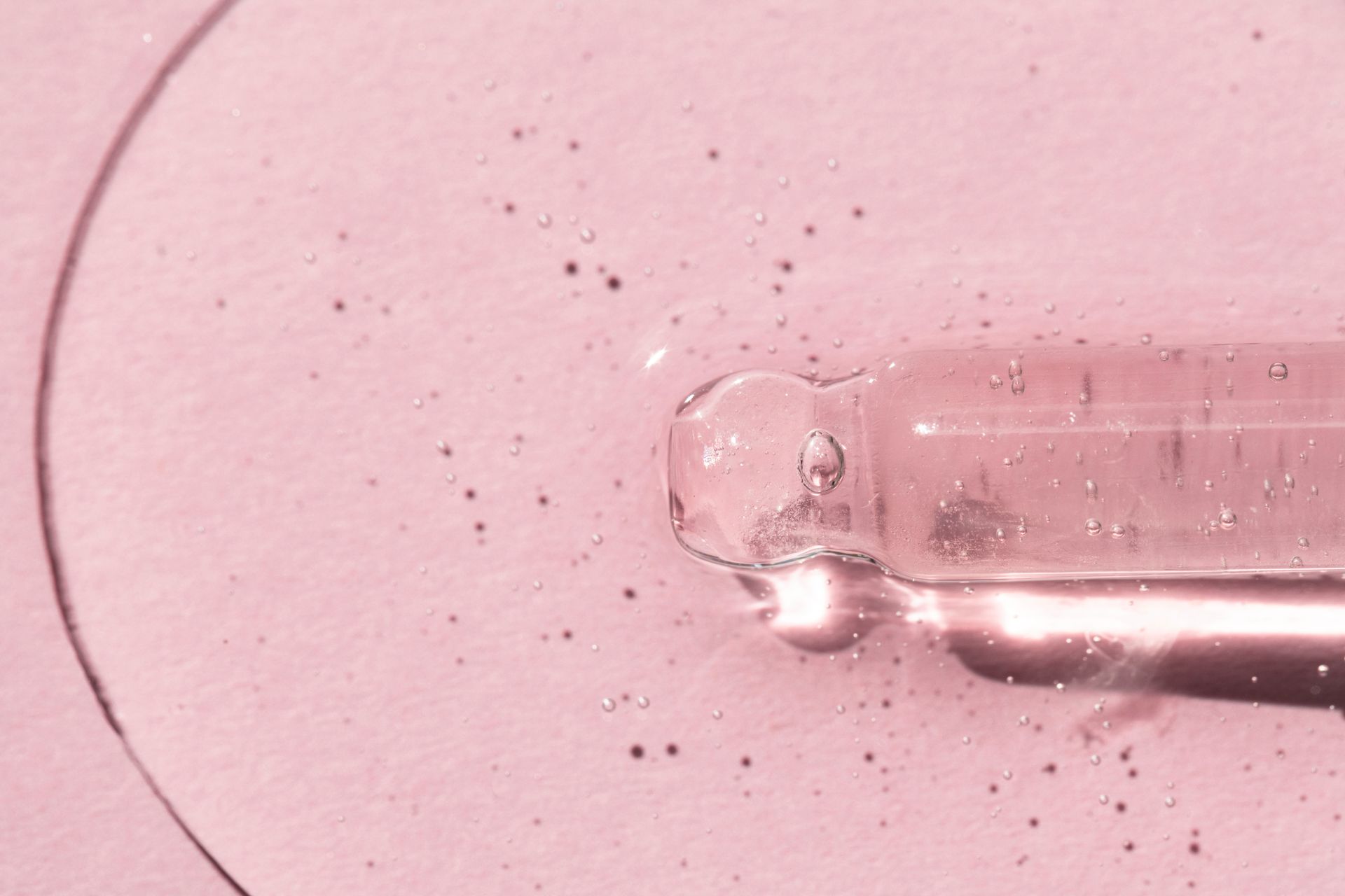 Eine Nahaufnahme einer mit Flüssigkeit gefüllten Pipette auf einer rosa Oberfläche.