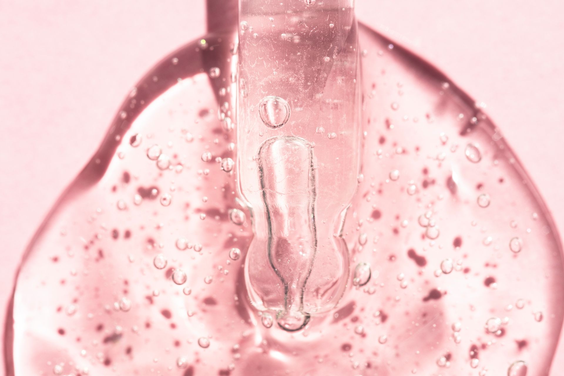 Eine Nahaufnahme einer Pipette mit einer rosa Flüssigkeit auf einem rosa Hintergrund.
