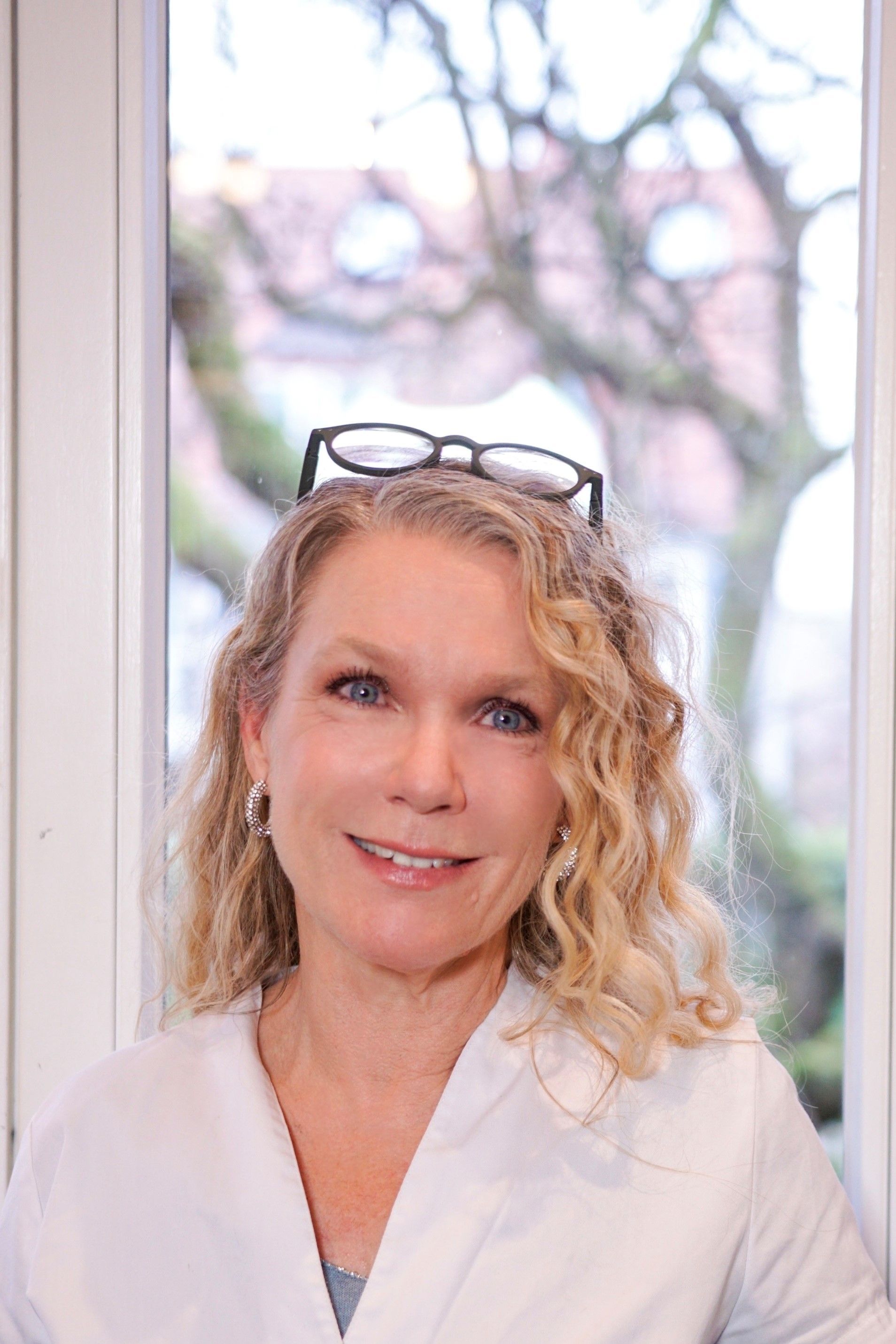 Eine Frau mit Brille und weißem Kittel steht vor einem Fenster.