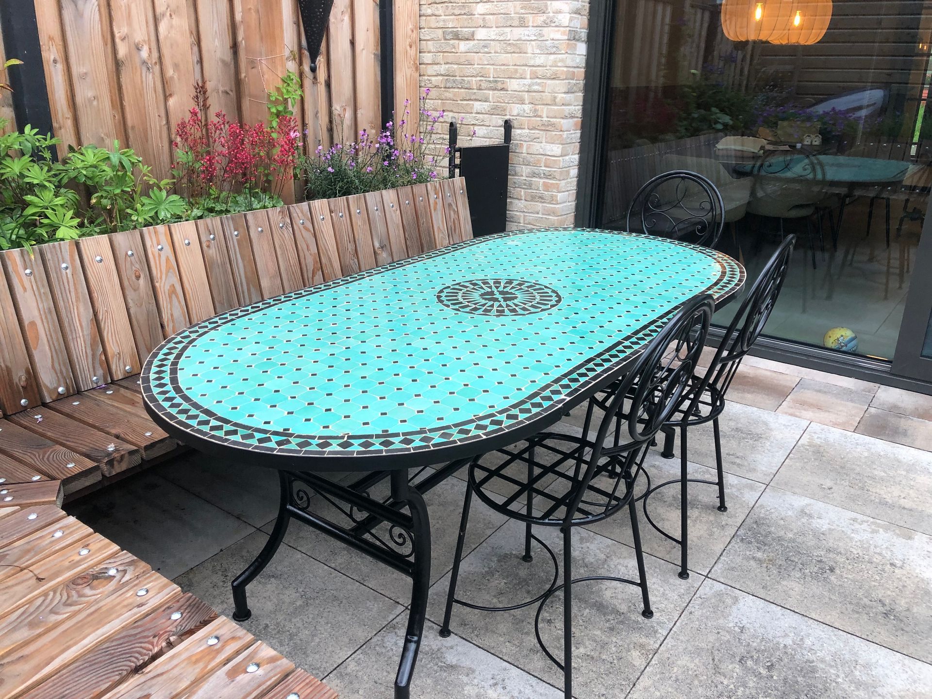 Buitenterras met Marokkaanse turquoise mozaïektafel, zwarte stoelen en houten schutting.