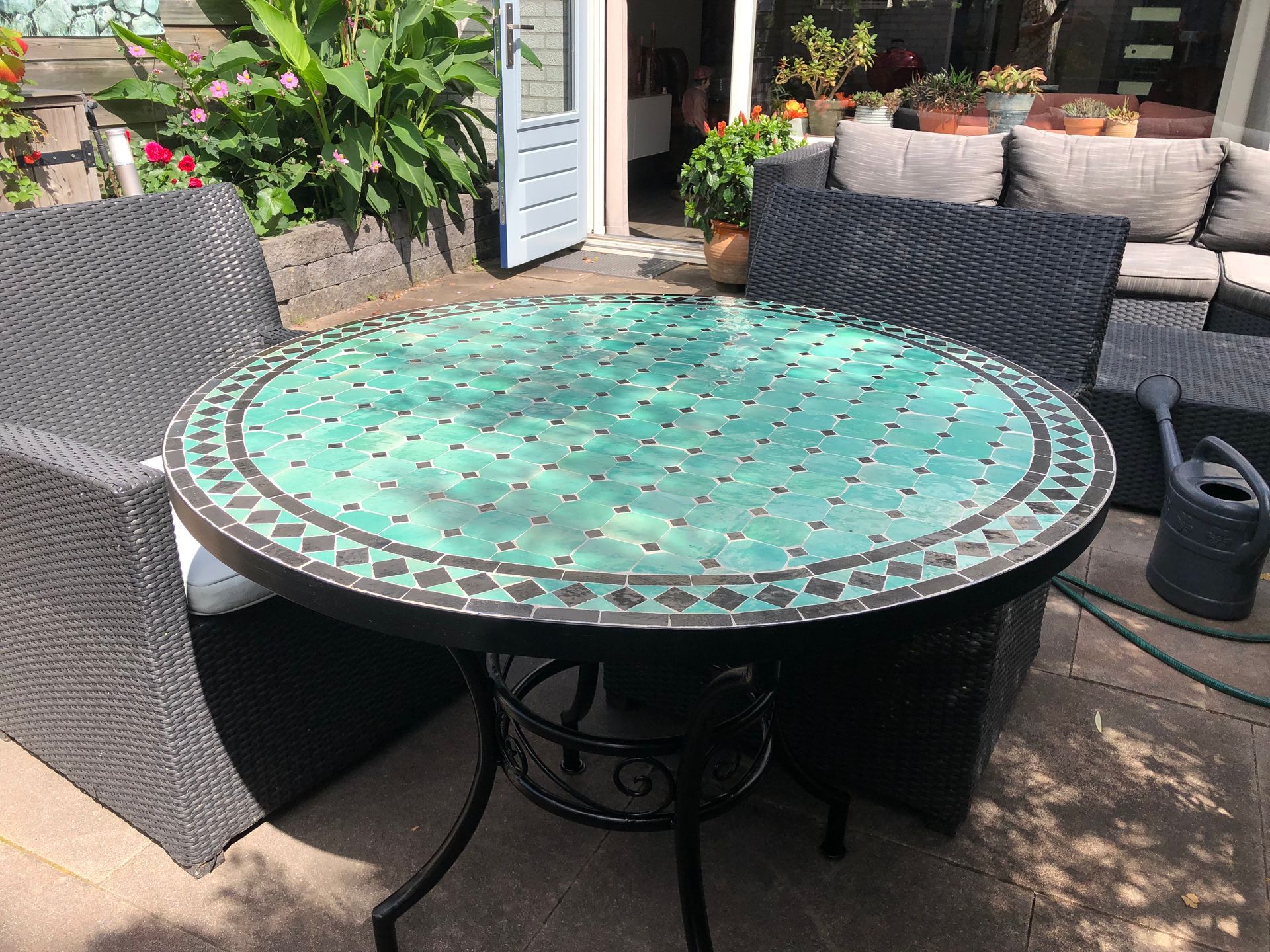 Terrastafel uit Marokko voor buiten met een turquoise mozaïekblad, omringd door zwart rieten meubilair.