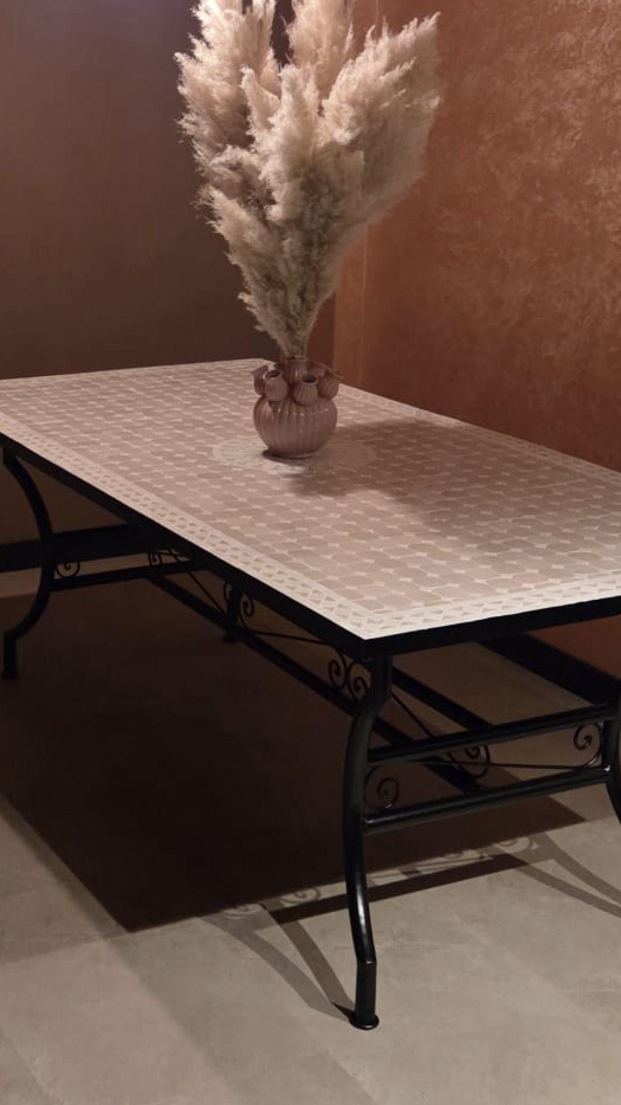 Marokkaanse mozaiek tafel  met een betegeld blad en zwarte metalen poten, waarop een vaas met pampasgras staat.