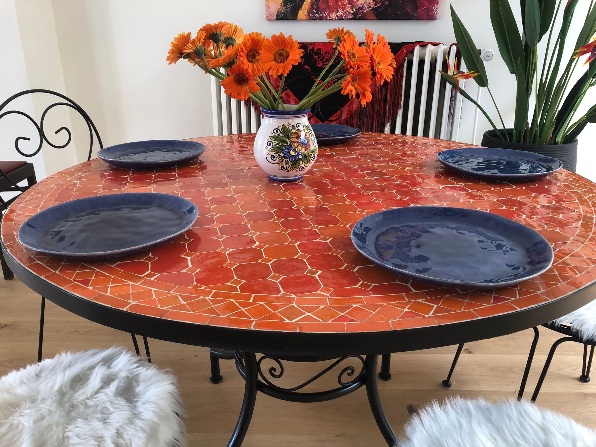 Ronde oranje Marokkaanse mozaïektafel gedekt met blauwe borden en oranje bloemen.