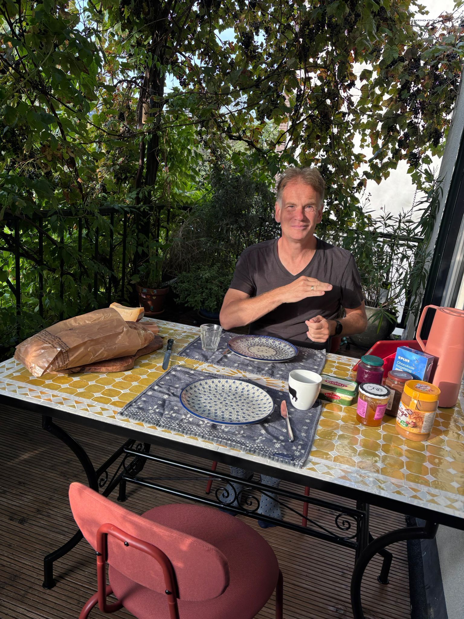 Een man zit aan een marokkaanse  tafel die buiten is gedekt voor het ontbijt en gebaart. 