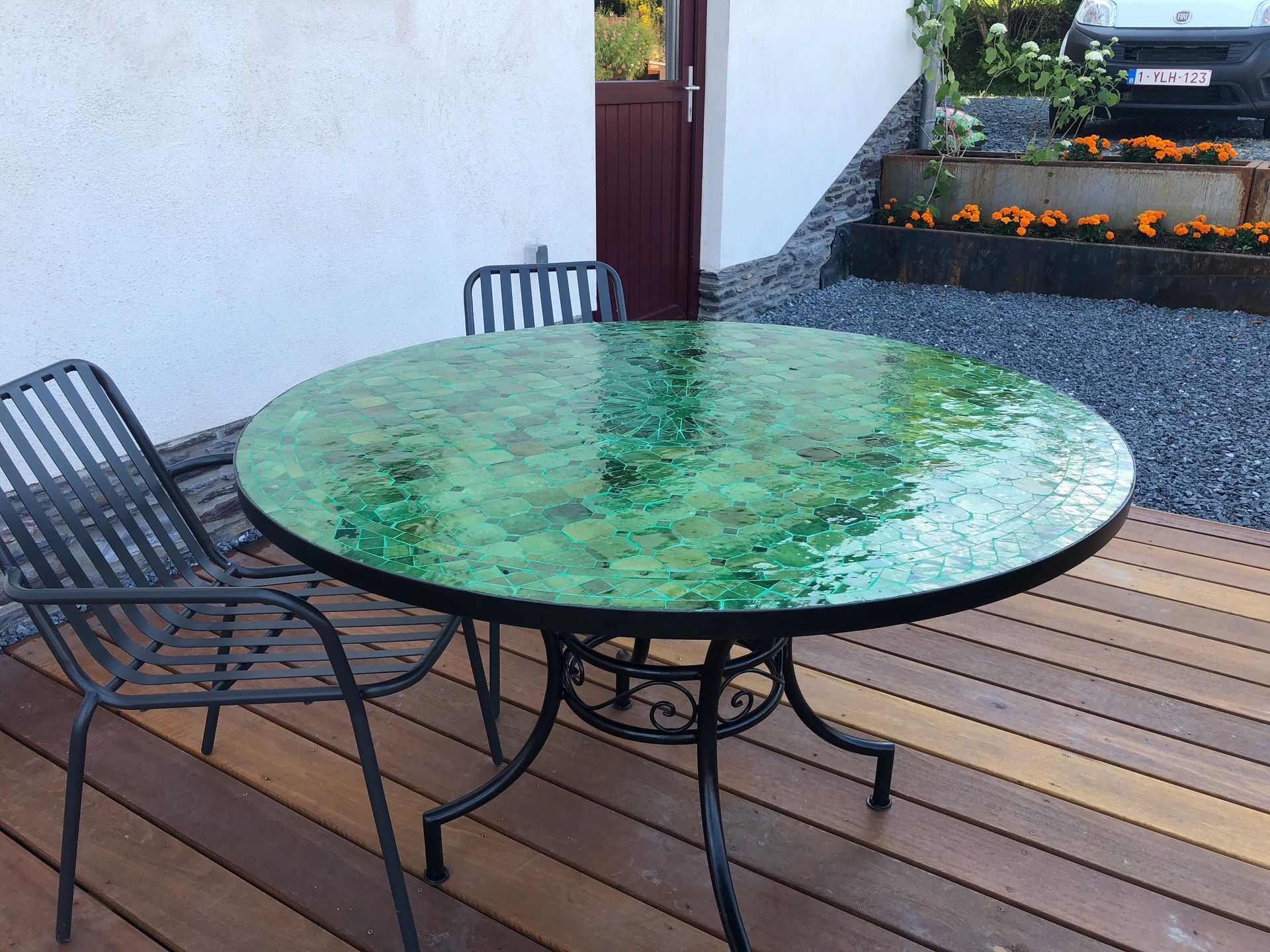 Ronde Marokkaanse tafel met een groen mozaïekblad en twee metalen stoelen op een houten vlonder.