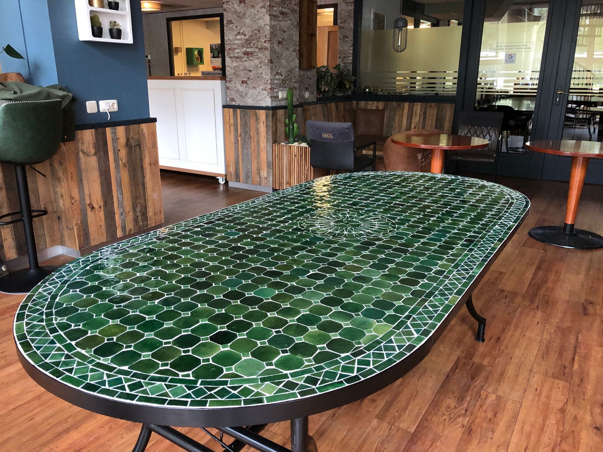 Een prachtige  groene Marokkaanse mozaïektafel , met een donker metalen frame, houten vloer en diverse zitgedeeltes.