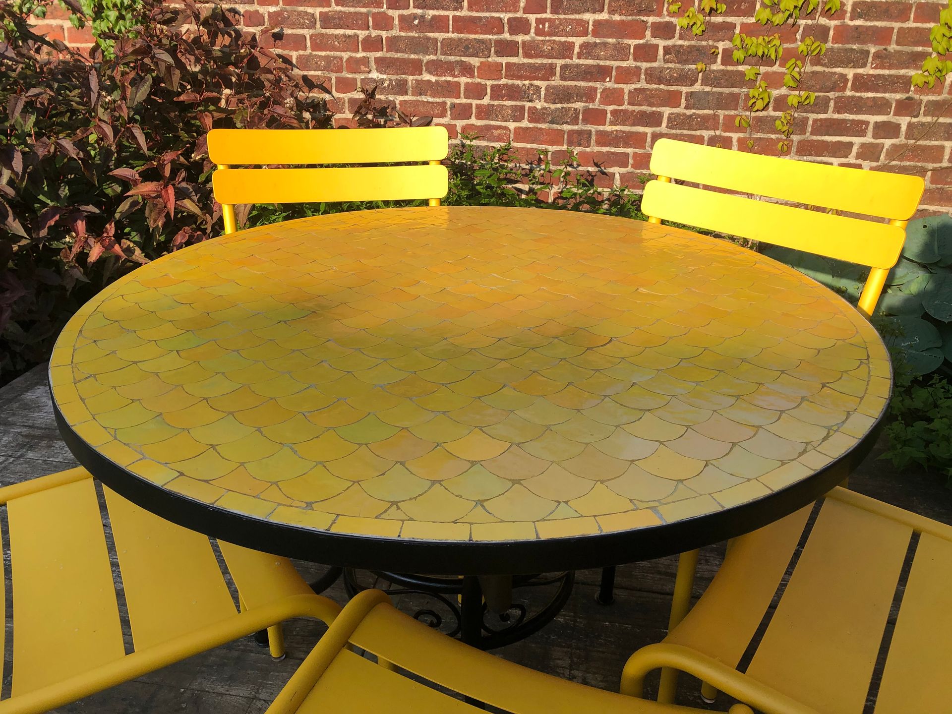 Gele Marokkaanse mozaiek tuintafel met stoelen voor een bakstenen muur.