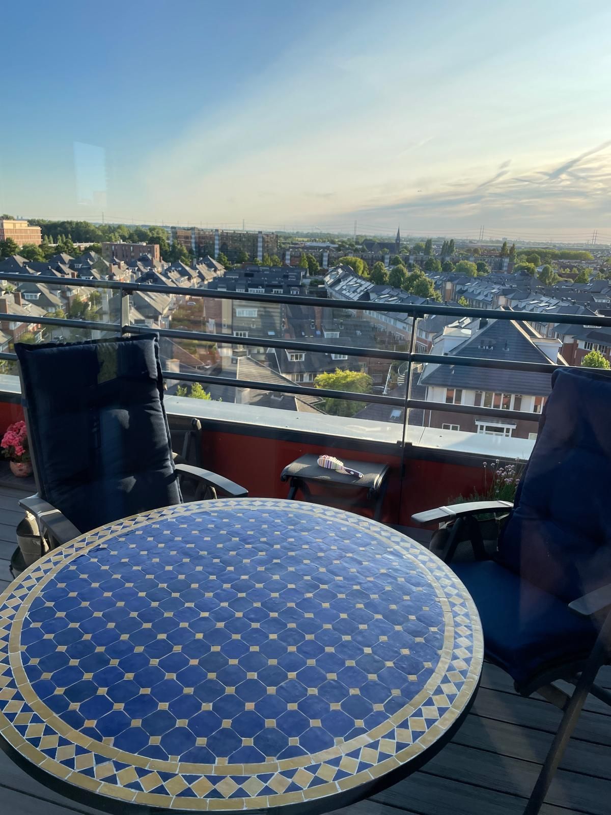 Balkon met een Marokkaanse mozaiektafel en twee stoelen in blauw mozaïek, met uitzicht op de stad onder een blauwe hemel.