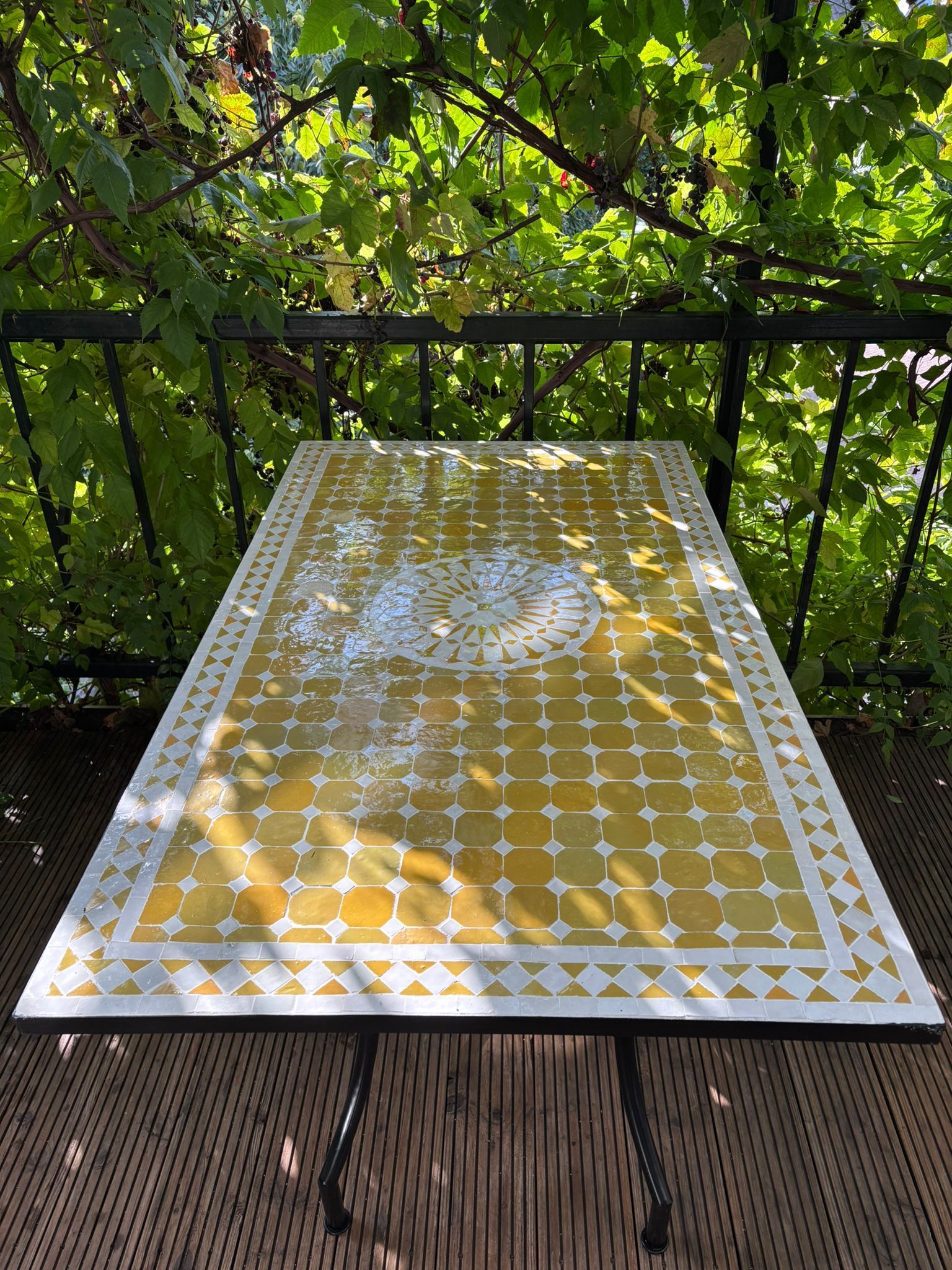 Een geel-wit  Mozaiek tafel uit Marokko tafel op een balkon met een groene, bladerrijke achtergrond.