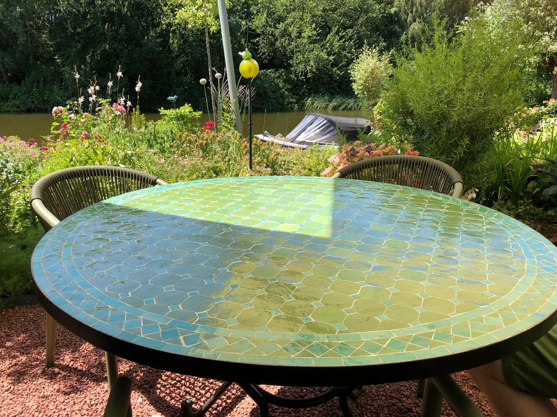 Ronde Marokkaanse mozaïektafel met twee stoelen op een terras met een weelderige tuin op de achtergrond.