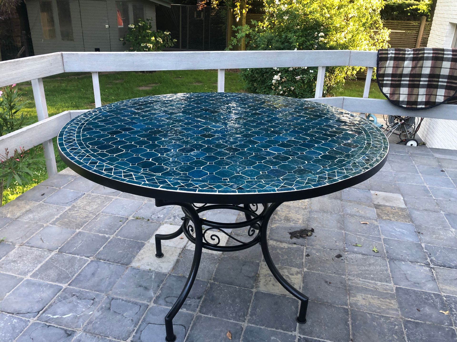 Ronde  Marokkaanse terrastafel met een blauw mozaïekblad en zwarte smeedijzeren poten, op een stenen terras.