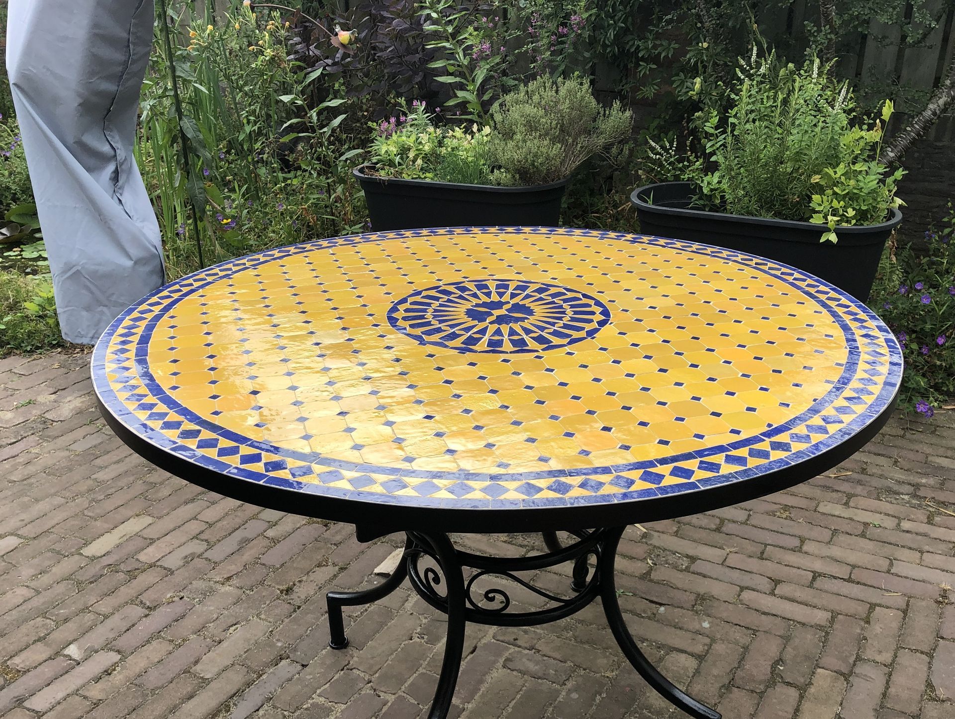 Ronde Marokkaanse mozaiektafel met een geel mozaïekblad en een zwart metalen onderstel.
