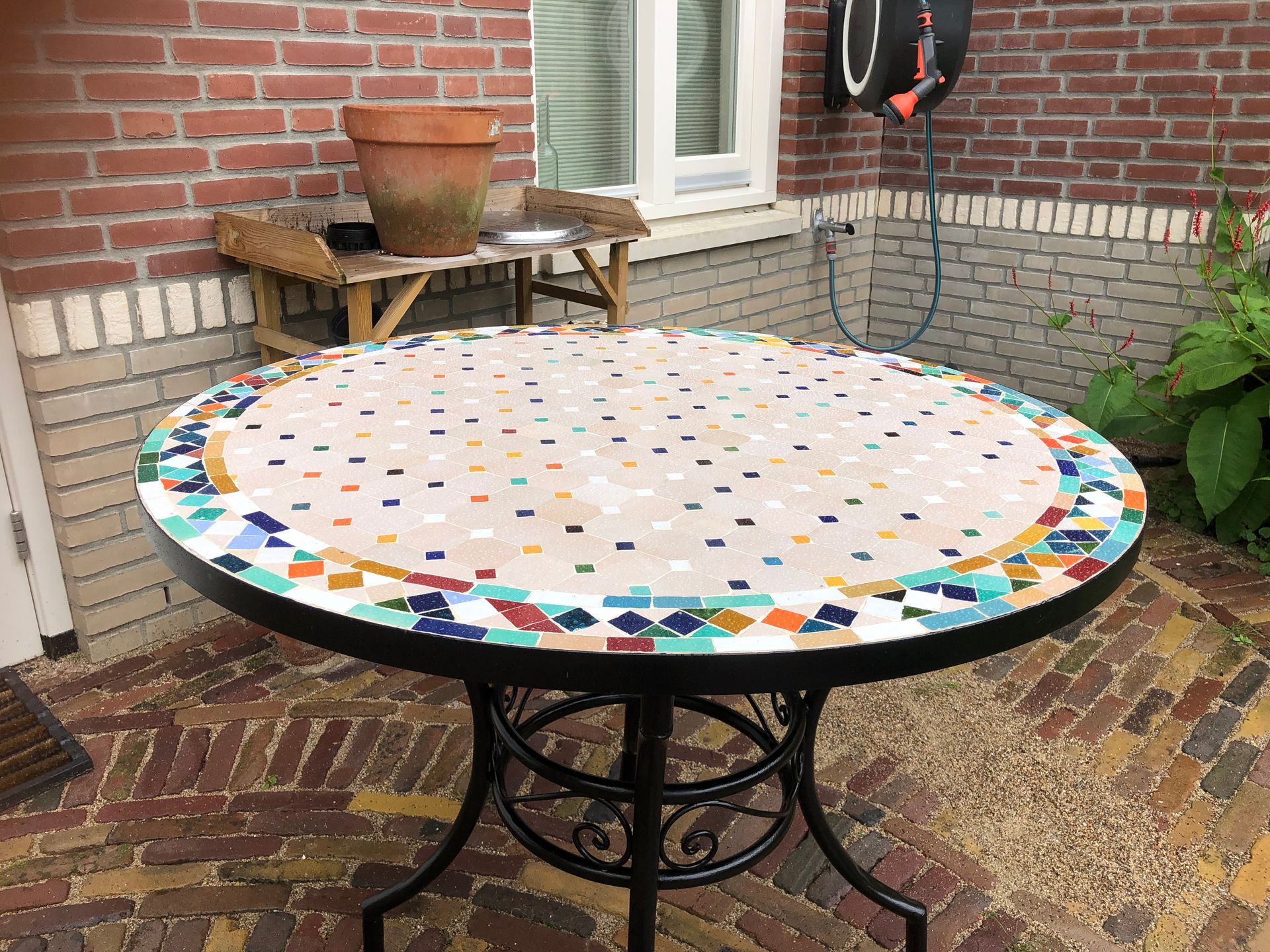 Ronde  Marokkaanse mozaiek tafel  met mozaïektegels op een zwart metalen onderstel, buiten op een stenen terras.