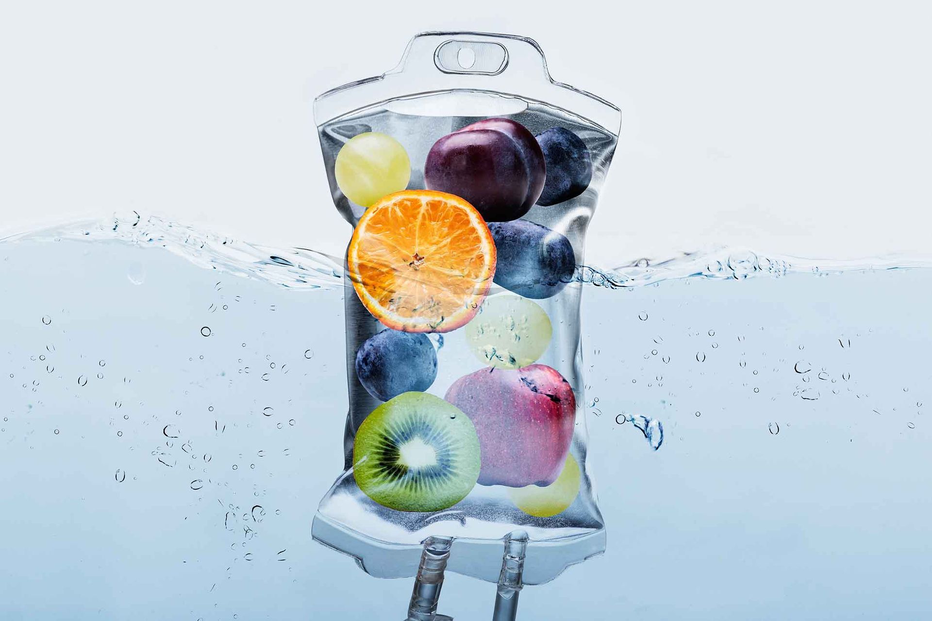 IV drip bag with fluid, tubing, and regulator against a blurred green leafy background.