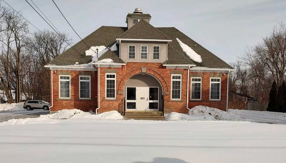 A red-brick building with a central arched entrance, dormer windows, and a cupola, set against a snow-covered landscape.