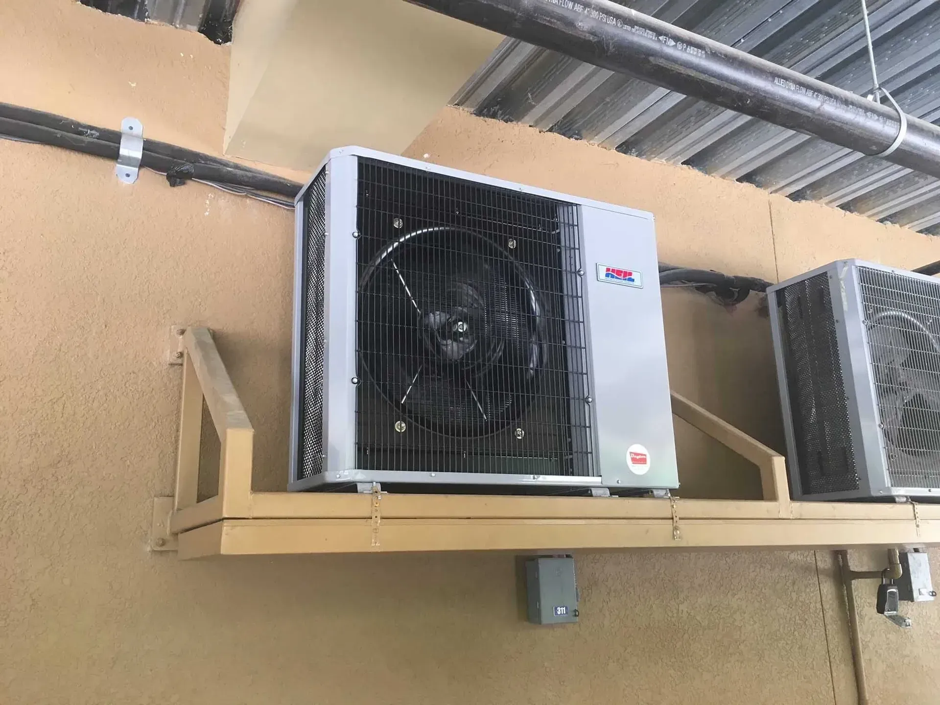 Air conditioning unit mounted on a beige wall, next to another similar unit.