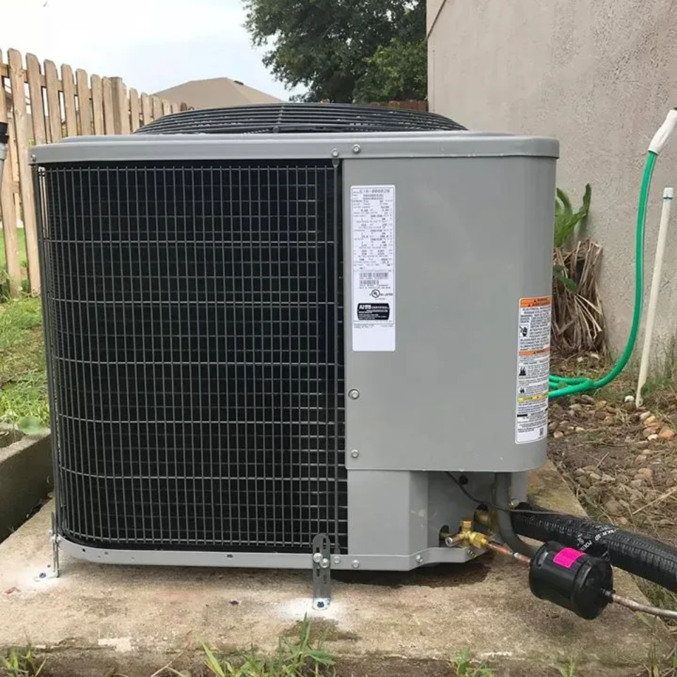 Gray air conditioning unit outside a building with a hose nearby.