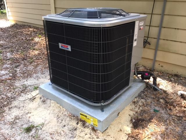 Air conditioning unit on a concrete pad near a beige building.