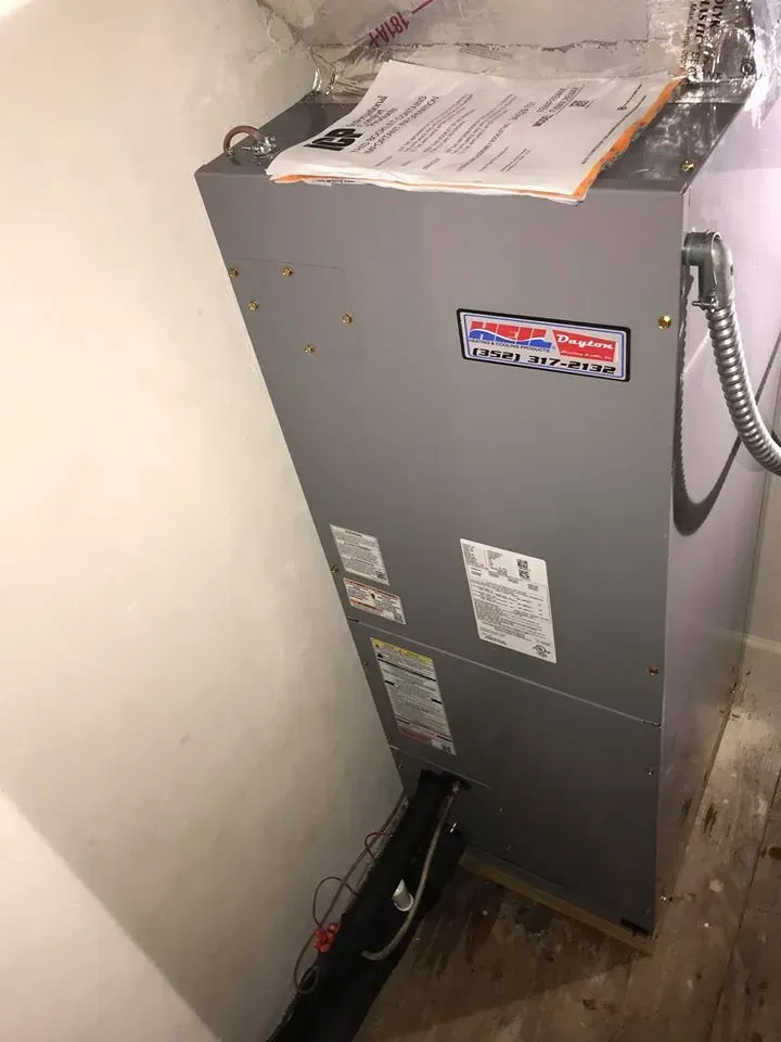 Gray furnace in a corner with black ductwork and papers on top.