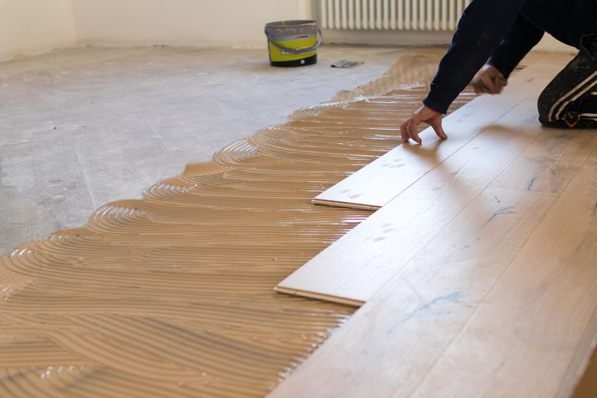 Person installing wood flooring, spreading glue on the subfloor.