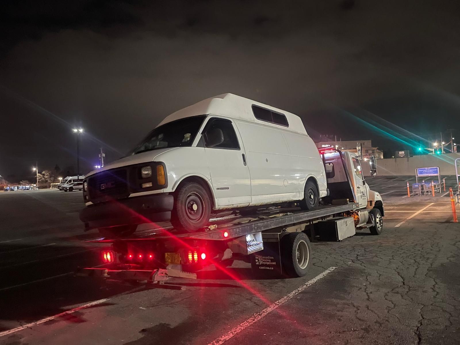 White van strapped to a flatbed tow truck at night in a parking lot